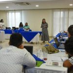 Mujer hablando a personas que se encuentran en recinto