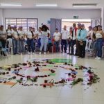 Mujeres rodeando espiral de flores con mensajes escritos en hojas de papel en el piso