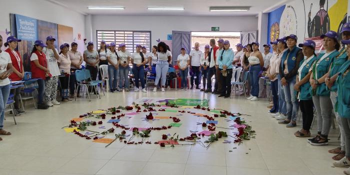 Mujeres rodeando espiral de flores con mensajes escritos en hojas de papel en el piso