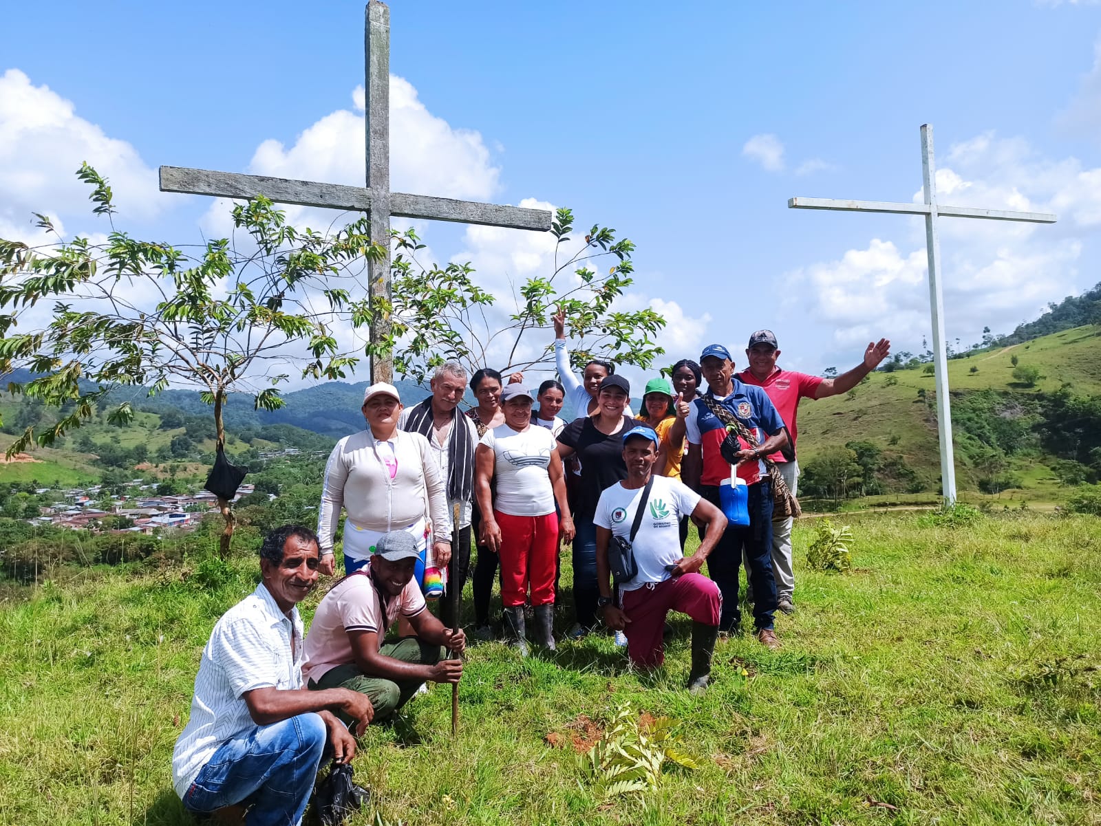 14 de personas posando para foto en zona rural con dos cruces cristianas en el fondo