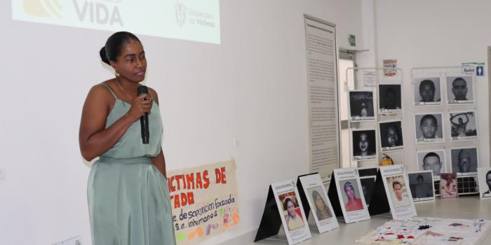 Mujer con micrófono hablando en acto simbólico con fotos de víctimas
