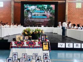 Mesa de participantes y mesa con fotos de victimas en audiencia por ejecuciones extrajudiciales