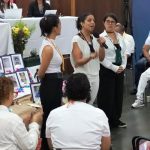 Mujer joven hablando por micrófono frente a personas en escenario de la JEP