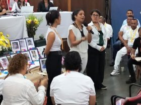 Mujer joven hablando por micrófono frente a personas en escenario de la JEP