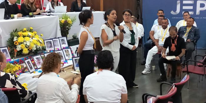 Mujer joven hablando por micrófono frente a personas en escenario de la JEP