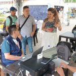 Dos funcionarios con computadores portátiles sentados en una mesa brindando información a mujer