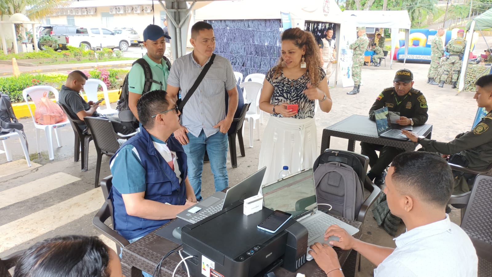 Dos funcionarios con computadores portátiles sentados en una mesa brindando información a mujer