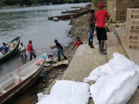 Personas desembarcando cajas ubicadas en canoas a la orilla del rio