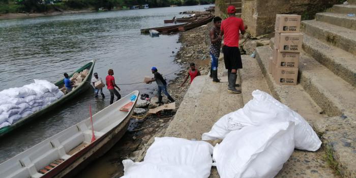 Personas desembarcando cajas ubicadas en canoas a la orilla del rio