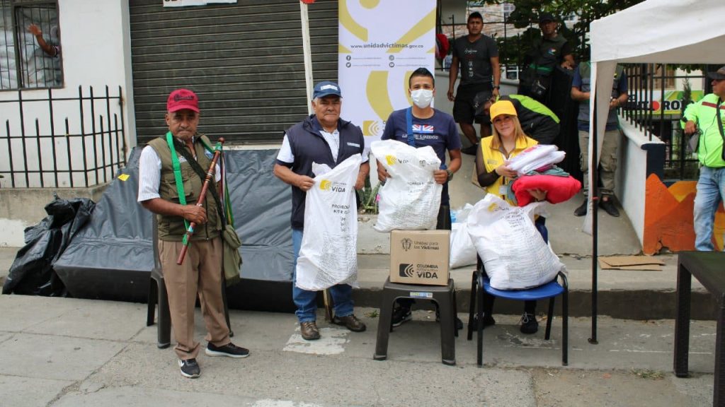 Grupo de personas recibiendo ayudas humanitarias en tulas blancas y cajas
