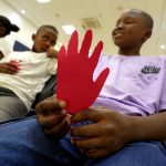 Tres niños sosteniendo una mano roja de carton