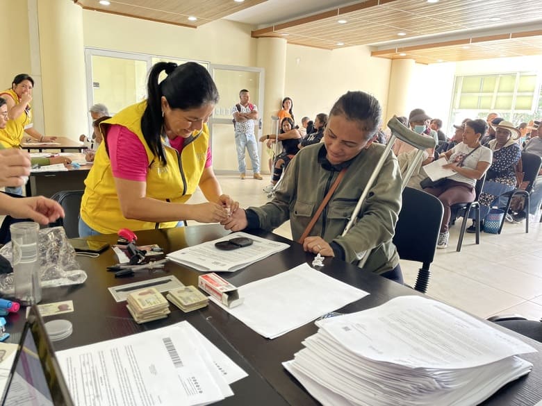 Funcionario con chaleco amarillo entrgando documento a mujer adulta